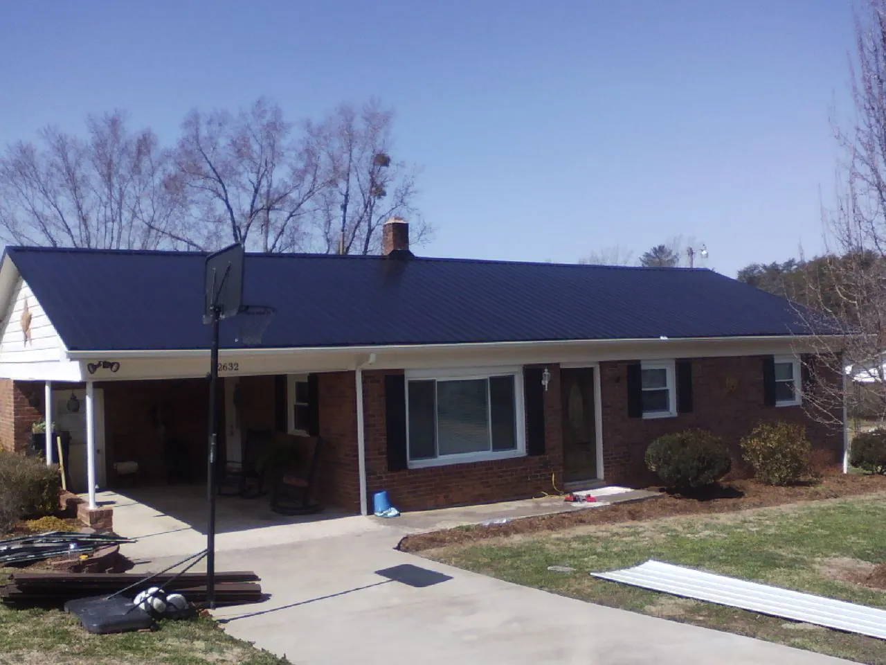 Finished dark blue metal roof on a brick ranch with a carport in Pocasset