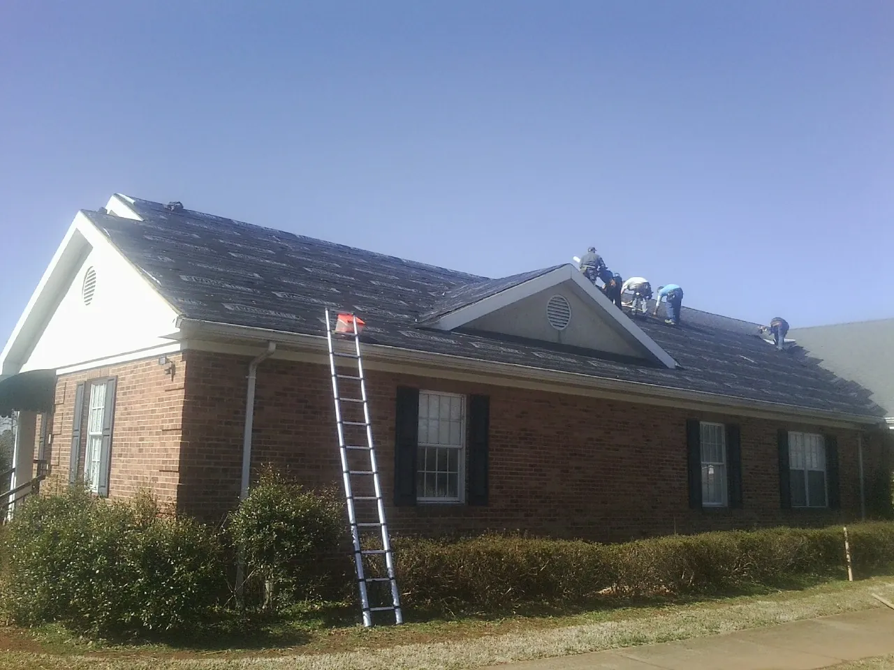 Crew tearing shingles off a brick ranch roof with a ladder set — Emergency Roof Repair work by our crew in Pocasset