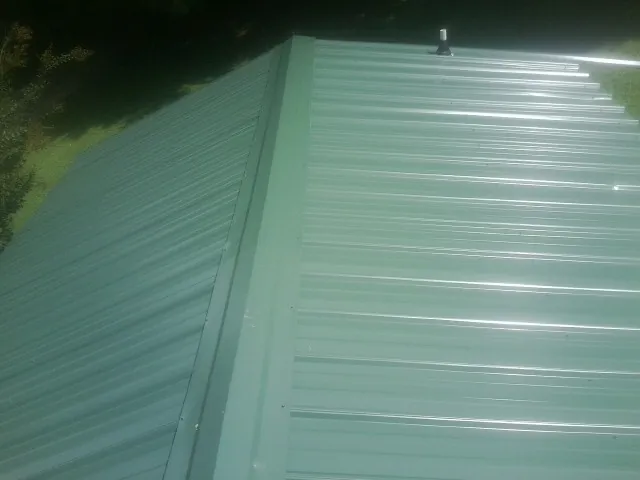 New green metal panels meeting at the ridge of a roof — Flat Roof Repair work by our crew in Pocasset