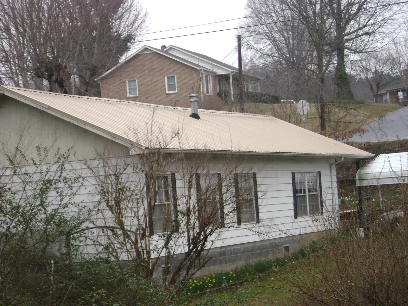 Tan metal roof on a white sided house set into a hillside — Commercial Roofing by Roofing Brothers in Pocasset