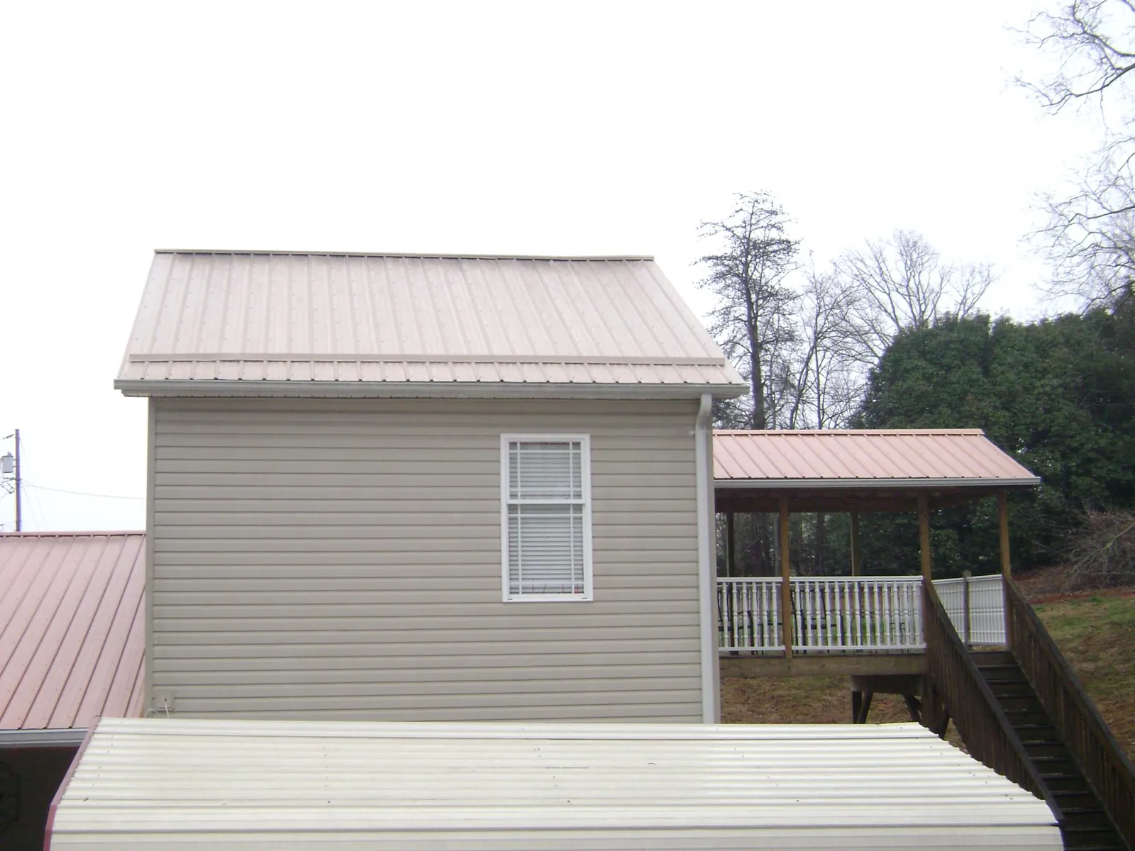 Tan metal roofs on a two story addition and attached porch, from a Roof Replacement job in Pocasset